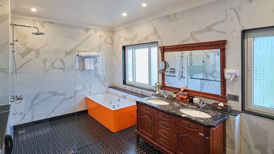 Royal Villa Bathroom with an orange bathtub, a walk in shower, a wooden cabinet with two sinks beneath a huge mirror