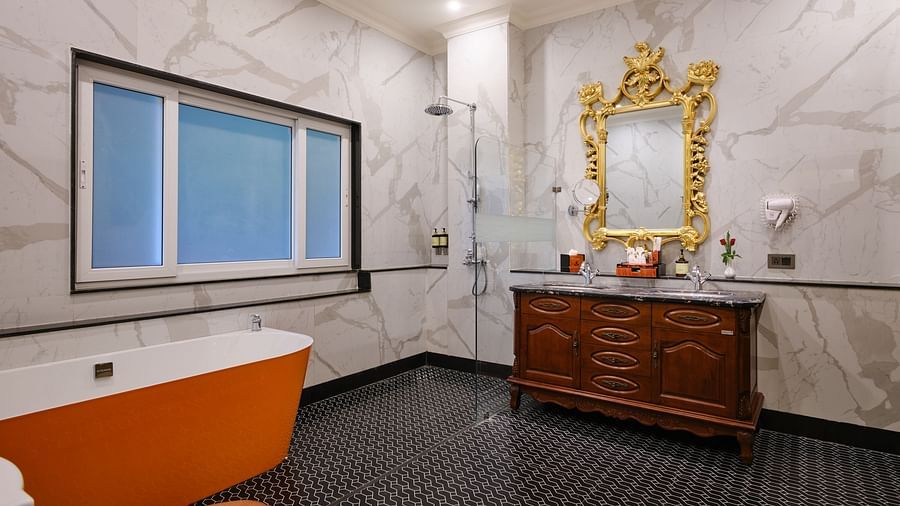 Suite Bathroom with an orange bathtub and a walk in shower against white tiled walls. A gold framed mirror above a wooden cabinet with two sinks 