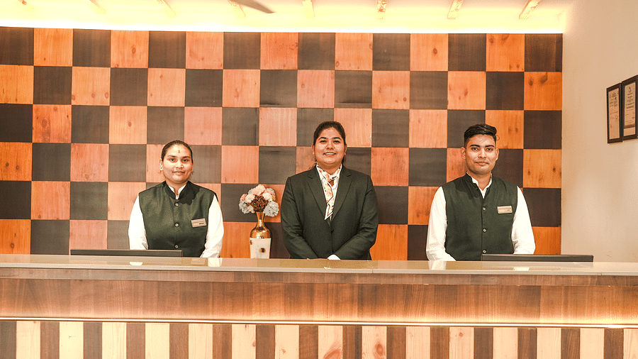 Hotel reception desk with smiling staff members in uniform, welcoming guests - Shervani Pebbles & Pines, Corbett