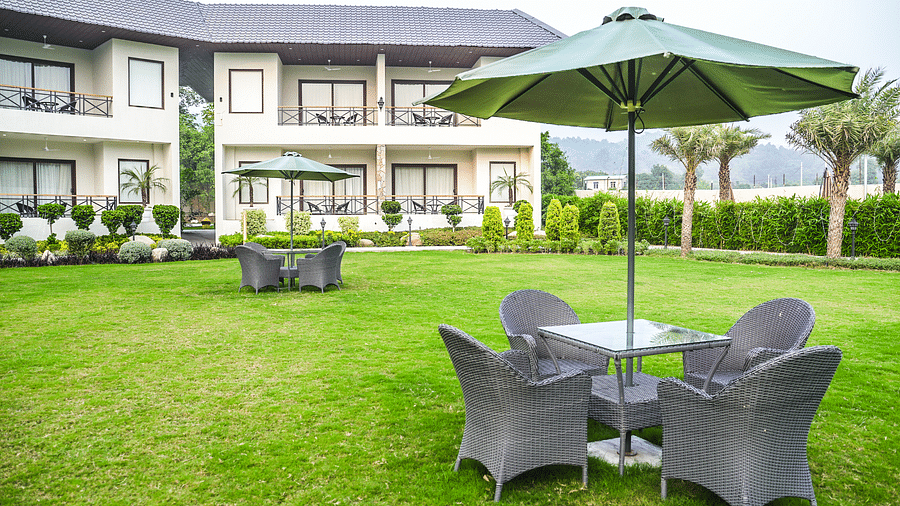 Outdoor seating area with wicker chairs and umbrellas, set against a lush garden and resort building backdrop - Shervani Pebbles & Pines, Corbett