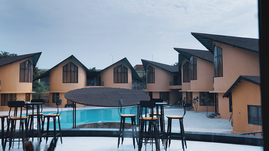 The Qualia Resort Club & Brewery, Udaipur with a pool at its centre is surrounded by modern buildings with distinctive rooflines, reflecting in the water.