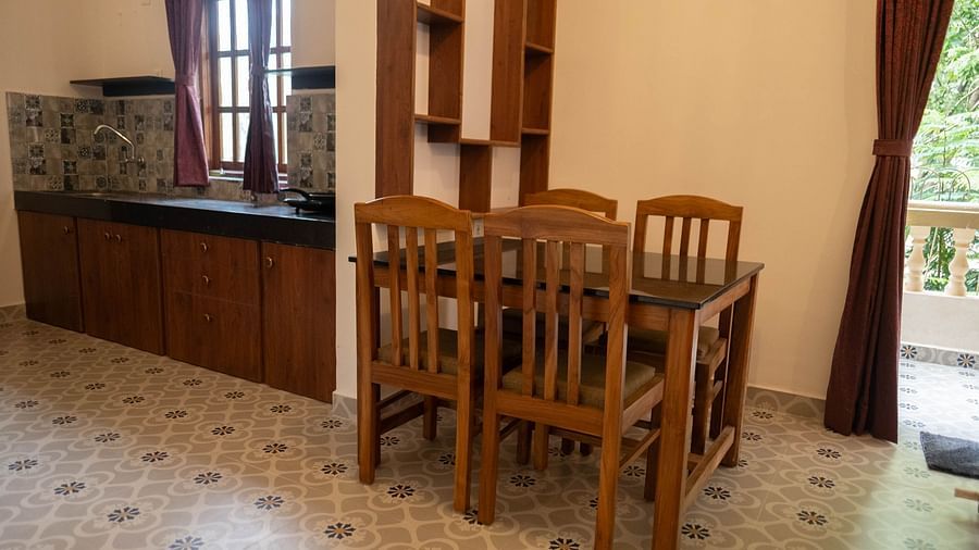Image of a dining table with chairs and a wooden shelf attached on the wall at Vistar, Holidays Goa.