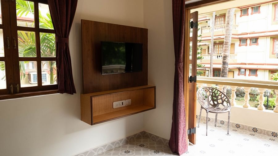 Image of a television mounted on the wall and a door leading to the balcony at the 1 bhk Executive Studio Apartment, Vistar Holidays, Goa.