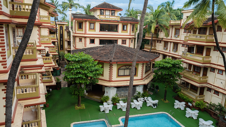 Facade of  Vistar Holidays, Goa with a swimming pool in front and chairs on the side of the pool.