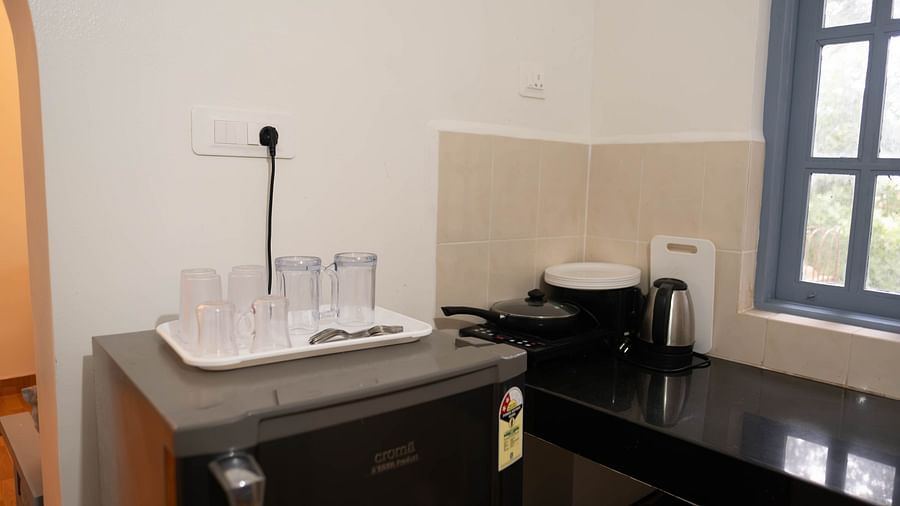 Image of a fridge with glasses placed on top and an induction and kettle on the table beside it at 1 bhk Deluxe Studio Apartment, Vistar Holidays, Goa.