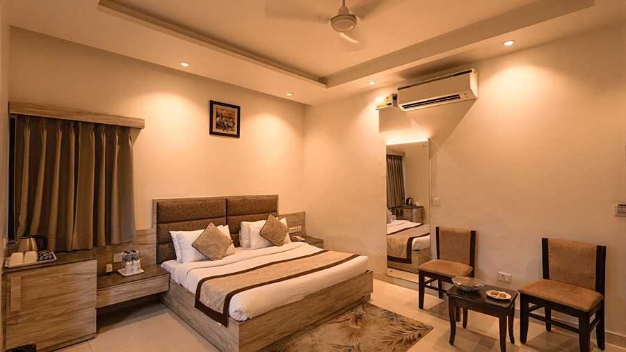 Warmly illuminated deluxe bedroom featuring a comfortable double bed and two wooden armchairs with a coffee table - Wood Castle Spa & Resort, Jim Corbett
