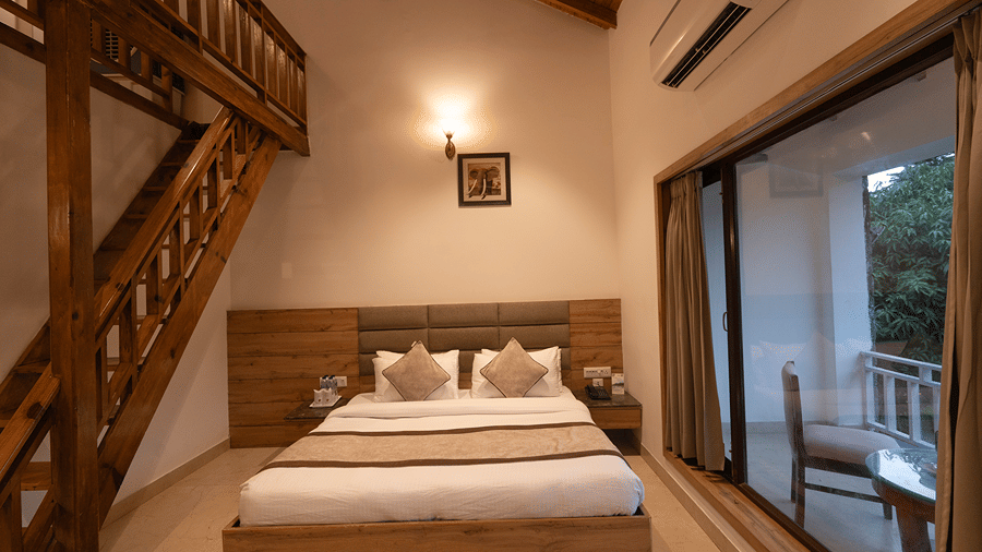 A plush double bed in a duplex cottage room with a wooden staircase and large glass doors leading to the balcony - Wood Castle Spa & Resort, Jim Corbett