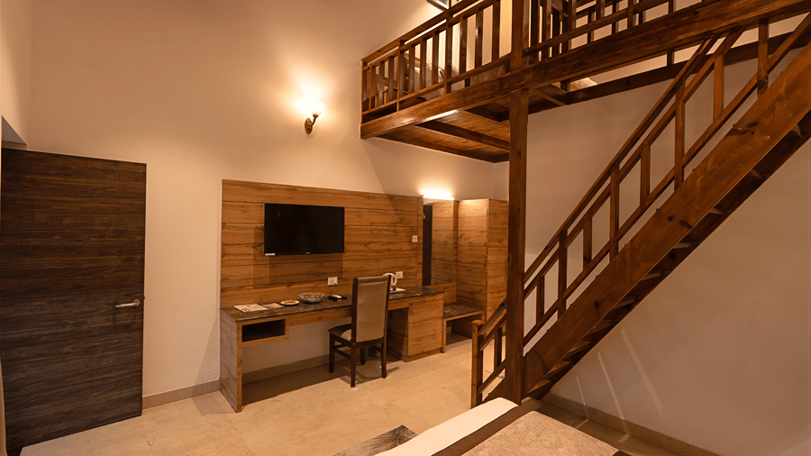 Interior of a duplex suite featuring a work desk, wall-mounted TV, and wooden staircase rising to the mezzanine floor - Wood Castle Spa & Resort, Jim Corbett