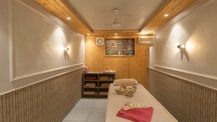 A cosy single massage room featuring a treatment table with folded towels, warm wall sconce lighting, and wood panelling - Wood Castle Spa & Resort, Jim Corbett