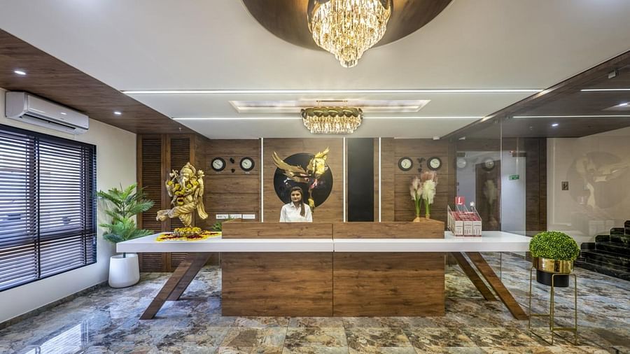 A well-lit hotel reception area with a wooden front desk and seating area towards the side at Angel Lords Eco Inn Amreli.