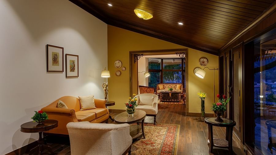 The living space with 3 sets of sofas and slanted ceiling made of wood, with two paintings nailed on the wall of a living area - The Naini Retreat, Nainital
