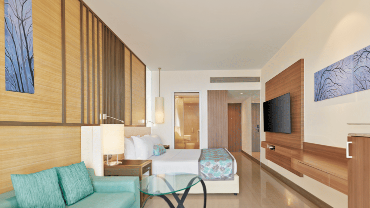 Stylish modern room with wooden accents, pastel furnishings, a wall-mounted TV and an open layout leading to a spacious ensuite – The Resort, Mumbai, the Best Place for Valentine's Day in Mumbai.