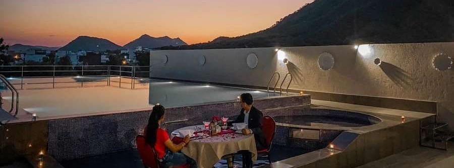 Rooftop terrace with mountain view, sunset sky, set tables.