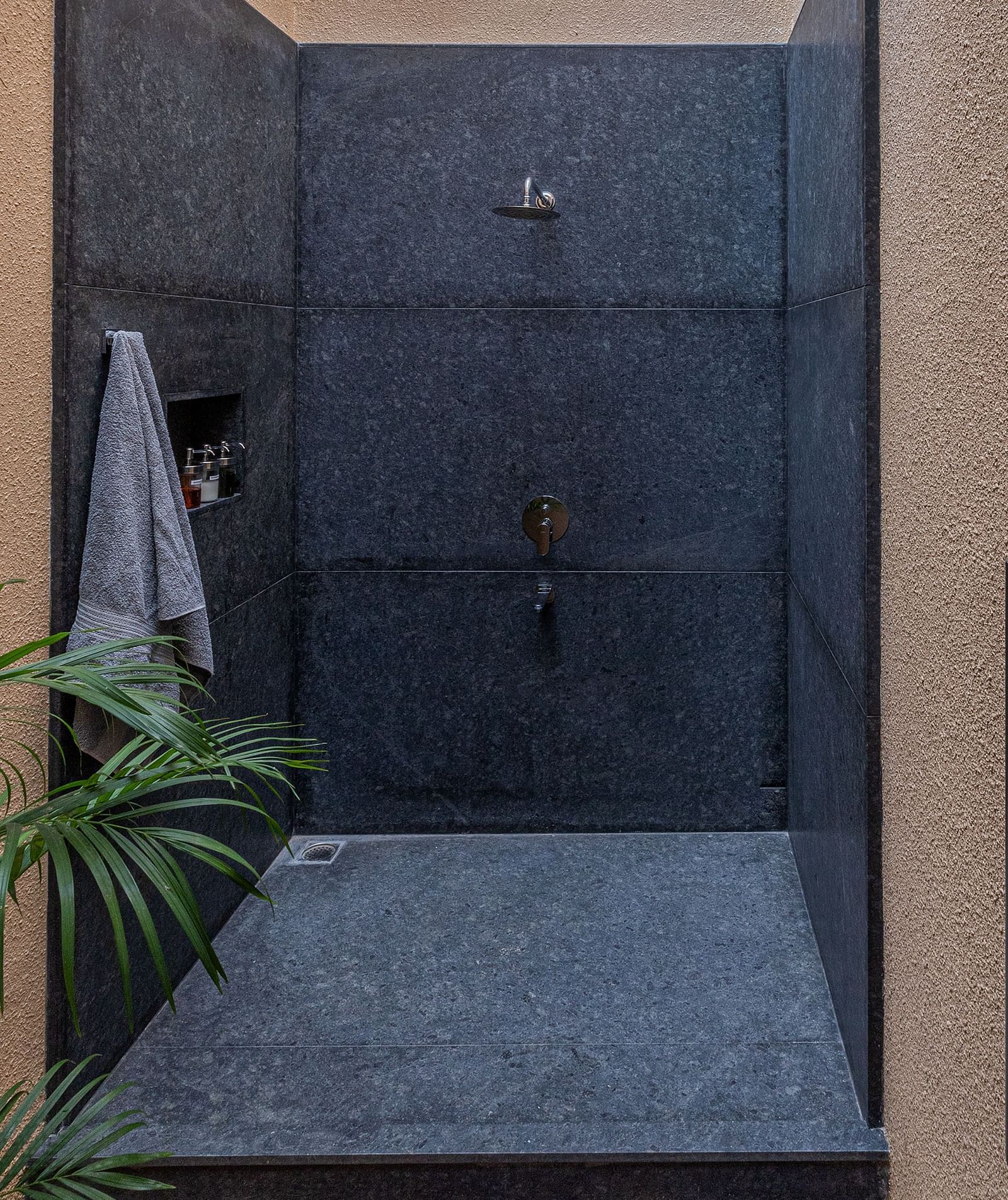 A narrow passageway with dark walls and a stone floor, plants visible at the end - Shreyas Retreat