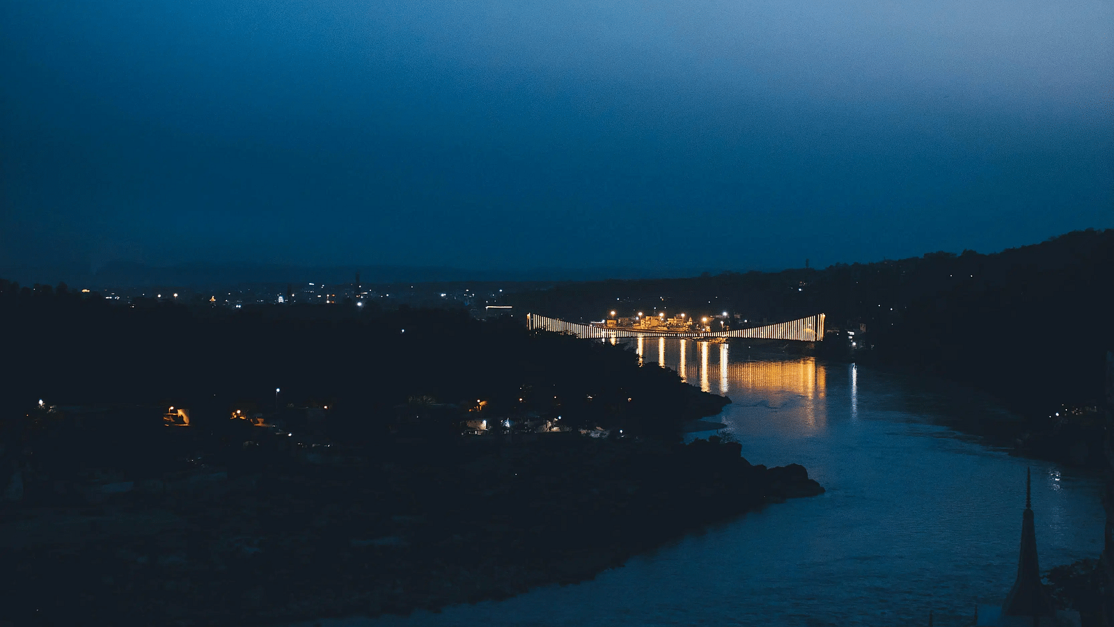 A vertical, low-angle shot of a dark body of water reflecting faint city lights under a deep blue twilight sky.