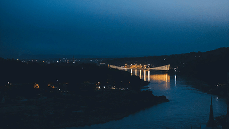 A vertical, low-angle shot of a dark body of water reflecting faint city lights under a deep blue twilight sky.