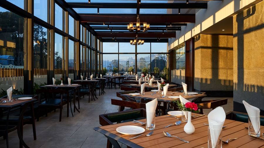 A rooftop dining view with variously arranged seating under an ambient lighting at The Hamuse Hotel, Kodaikanal.