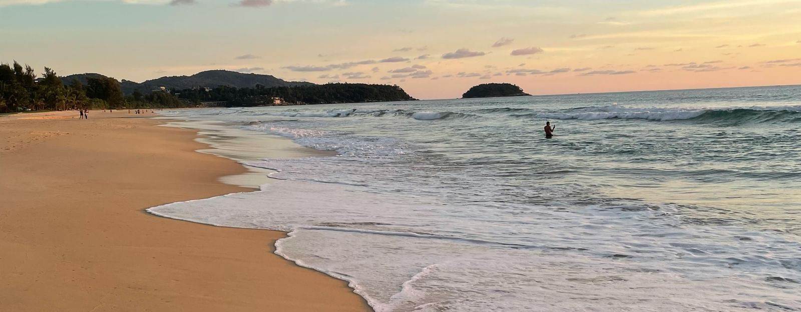 A beach scene at sunset with gentle waves washing onto the sandy shore.