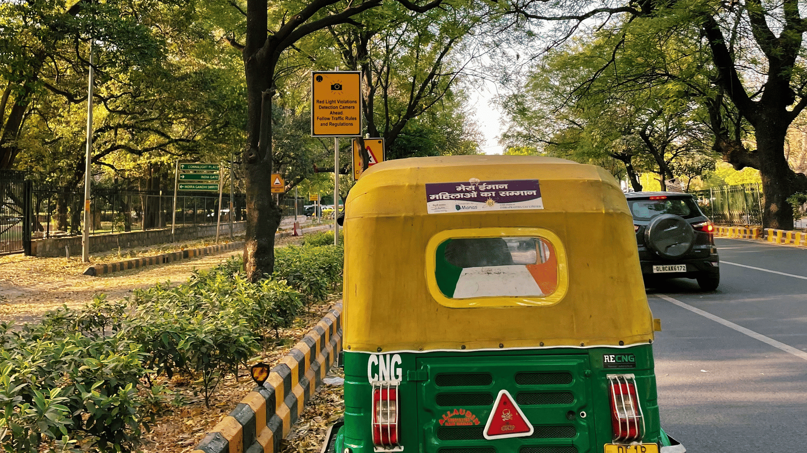 An auto-rickshaw near a tree-lined road with a pedestrian sign on the side