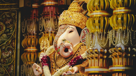 Ganpati idol decorated with floral garlands and gold ornaments beside intricately carved temple pillars at Shrimant Dagdusheth Halwai Ganpati Mandir.