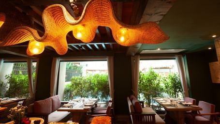 A wide-angle shot of the interior of the Mila Restaurant at The Evren, Vagator, highlighting the unique, woven light fixtures hanging from the wooden ceiling.