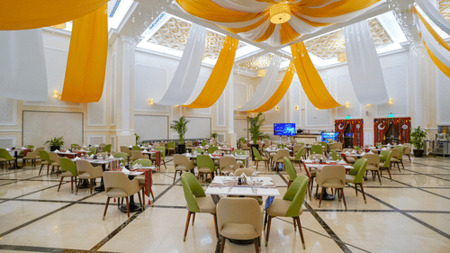Round table seating inside a banquet hall with white and orange cloth hanging from the ceiling as decoration - La Maison Hotel, Doha