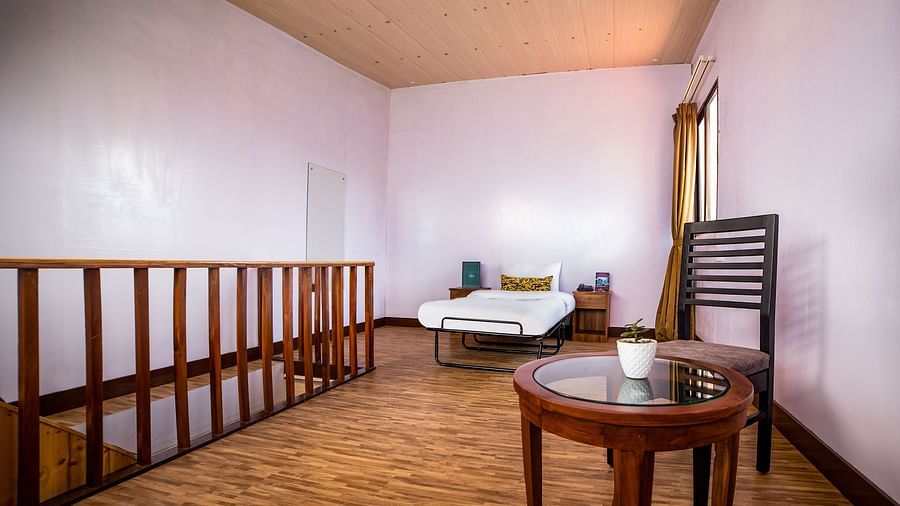 A loft-style room in Sumitel Hotel with a visible staircase, a single bed in the corner, wooden flooring, and a round table with a chair.