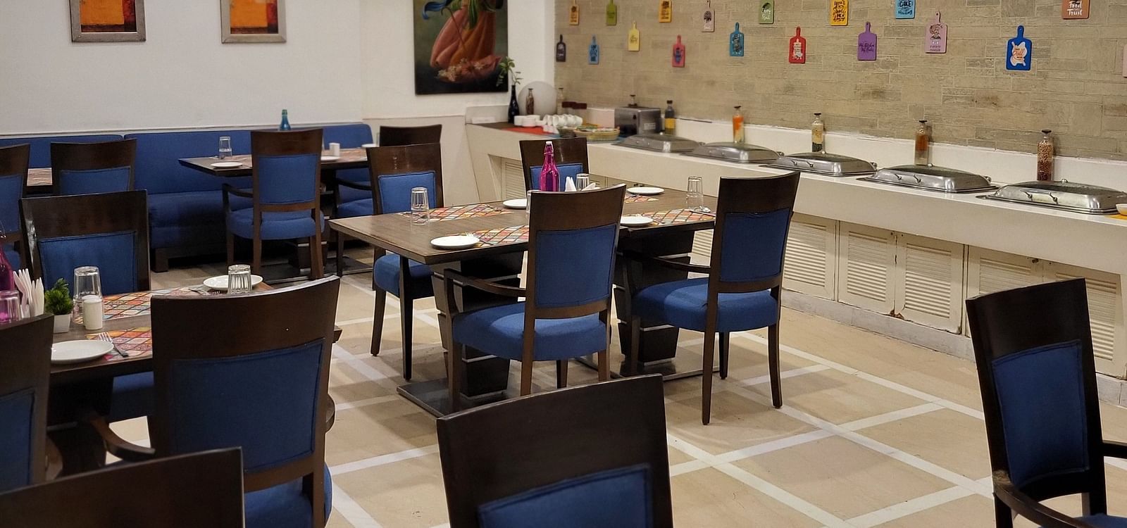 An image of a restaurant featuring multiple sets of chairs and tables where plates, cutlery and napkins are placed at Inde Hotel Signature Tower Gurgaon