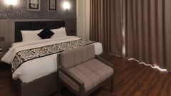 A room at Grand Continent, Anjuna featuring a large bed, a small sofa, dark curtains, and patterned walls with decorative lights.