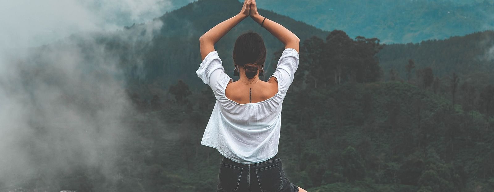 A woman does a yoga posture on a hilltop - monsoon and ayurveda - Gamyam Retreat