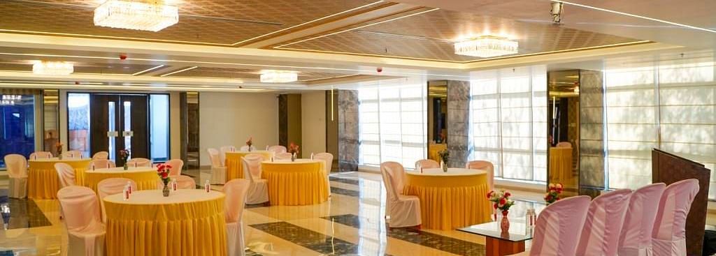 A grand banquet hall with round tables, a red stage, and white chairs, ready for an event, featuring ornate ceilings.