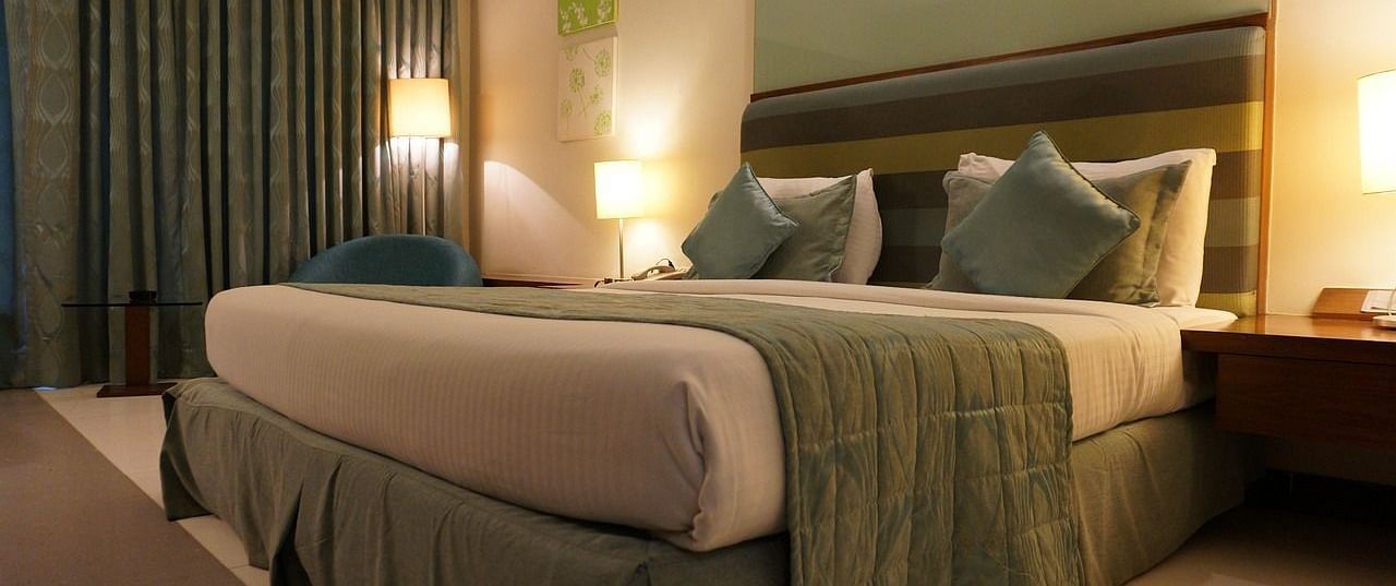 A double bed with pillows and cushions kept neatly against the head board of the bed in a warmly lit room.