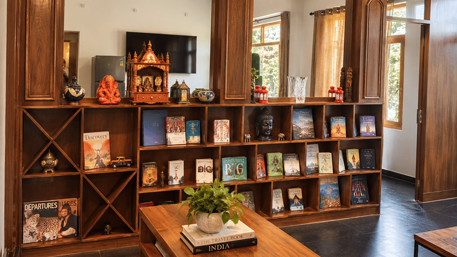 Mohan Chatti by Eastlynn Experiences reading nook with wooden bookshelves filled with books, a small coffee table, a wooden bench and a decorative idol.