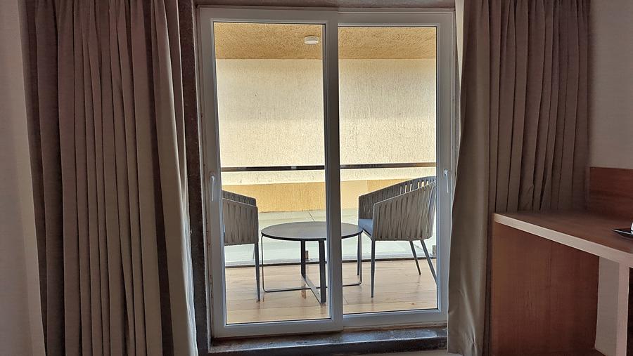 Room with glass balcony doors, curtains, wooden furnishings, and outdoor seating.