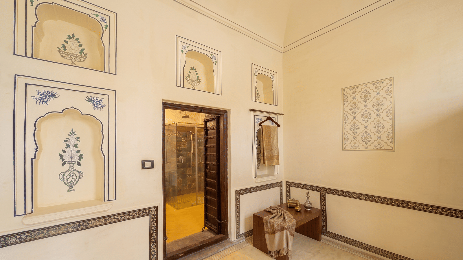 Dressing area with painted wall niches, a luggage bench and an open door to the tiled walk-in shower at BluSalzz Vintage - Harlalka Haveli.