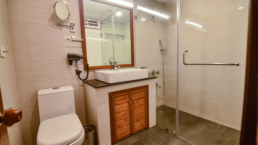 Contemporary bathroom featuring wooden vanity with mirror, toilet, and glass shower partition, tiled walls with recessed lighting at Cedar Inn.