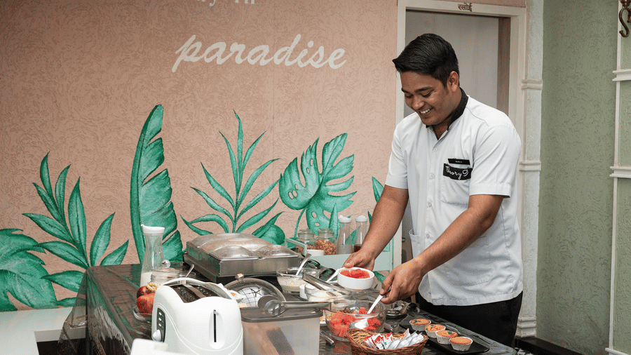 Chef preparing fresh dishes at Theory9 Premium Service Apartments, Bandra, inside a vibrant kitchen space with tropical wall art, showcasing the property’s personalised and homely culinary experience.