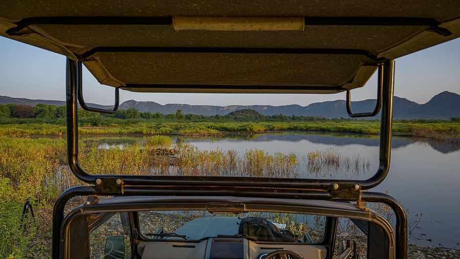 An image of the inside of a jeep over viewing a lake and the mountains -0 An image of a jeep parked amidst the rocky mountains - Utsav Camp Sariska