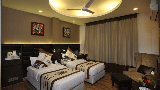 A Superior Twin Bed Room at JRD Exotica - Business Hotel featuring twin beds, an armchair with an ottoman, and modern lighting.