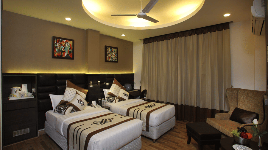 A Superior Twin Bed Room at JRD Exotica - Business Hotel featuring twin beds, an armchair with an ottoman, and modern lighting.