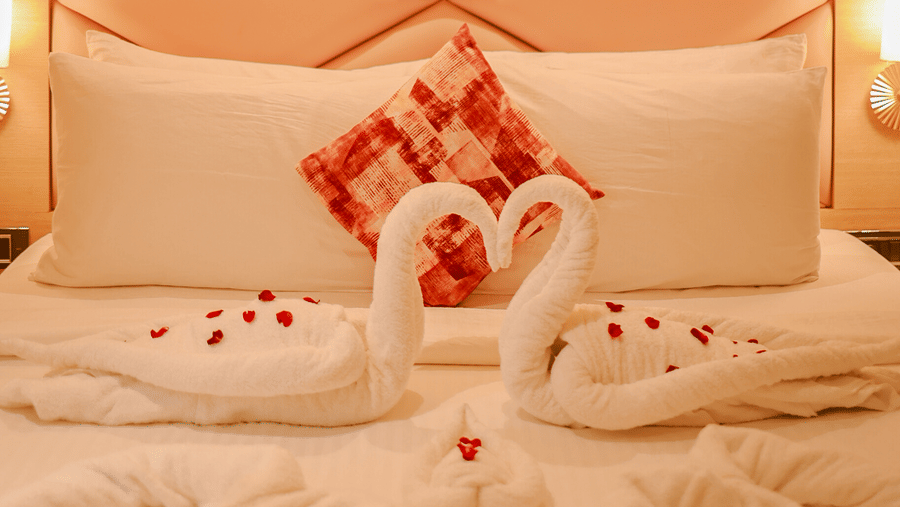 Bed with floral towel arrangement and illuminated headboard at Hotel Mumbai House Digha, Airoli.