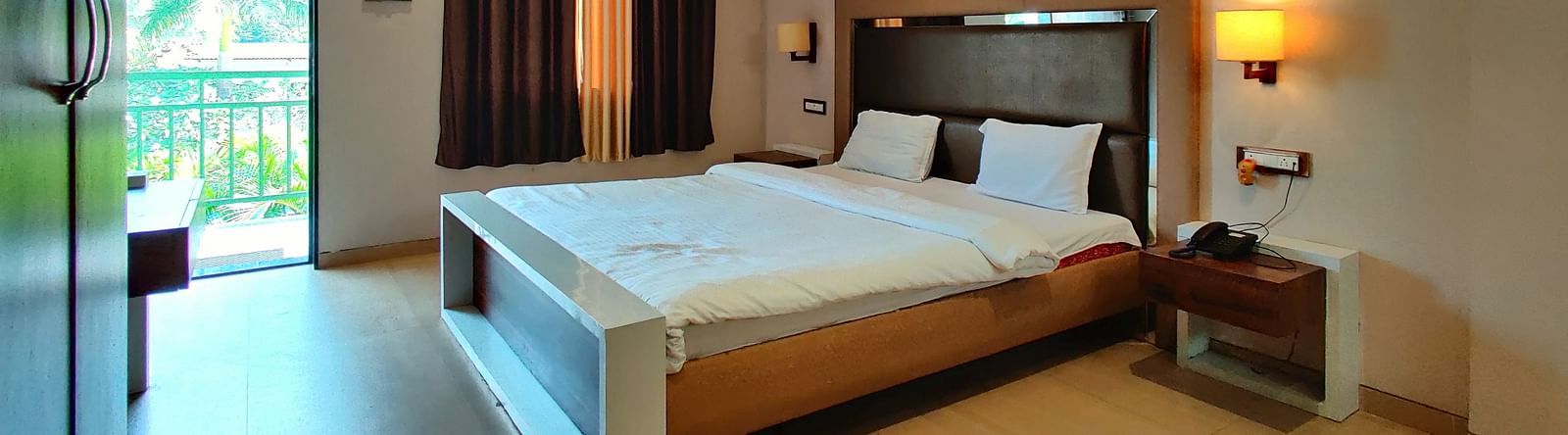 Overview of a Super Premium Room at The Kanila Resort with a queen sized bed, a nightstand, a TV, and a desk. 