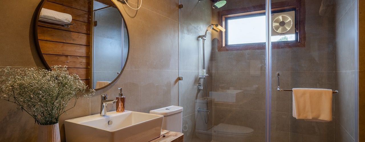 An image of a washroom with sink, faucet, mirror on the wall , shower screen, and a towel hanging inside the shower - Avalon Cottages, Kanatal