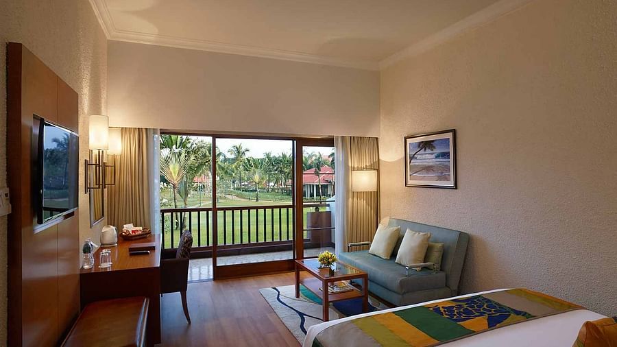 a double bed with a sofa in front of it and a tv wall mounted on the side inside garden-room in South Goa - Caravela Beach Resort, Goa