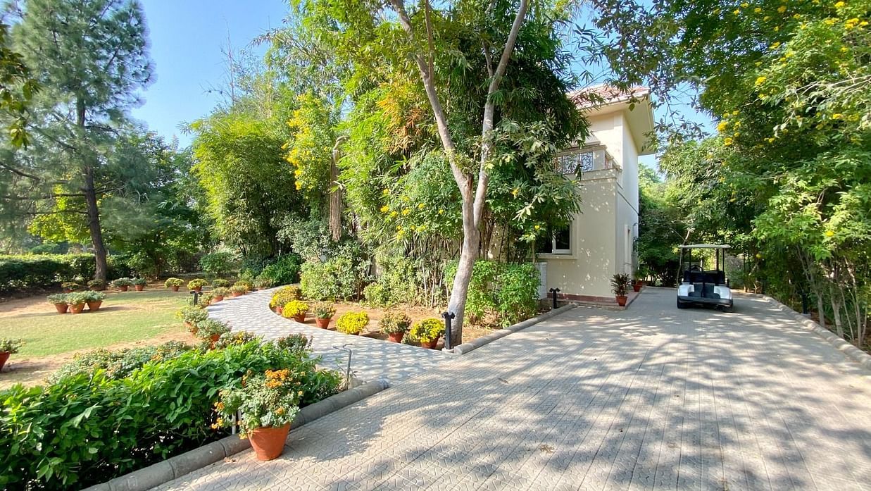 An image showing a huge house with green trees and lawn inside the compound, pictured with a golf cart parked on the front of the house
