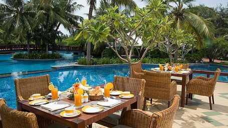 Water Edge Cafe- Poolside dining setup with a table adorned with a tropical feast, surrounded by palm trees and scenic views at GRT Hotel
