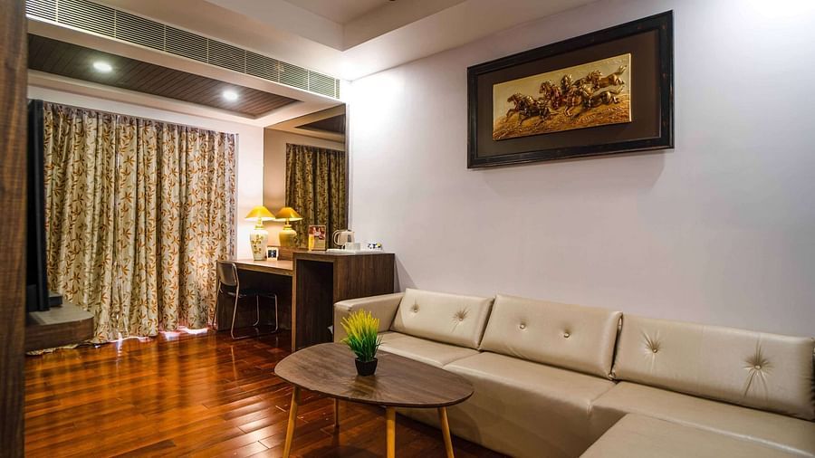 A spacious room Mansha Hotel Regency offering a sofa, a coffee table, a work desk, a chair, and an artwork hung on the wall.