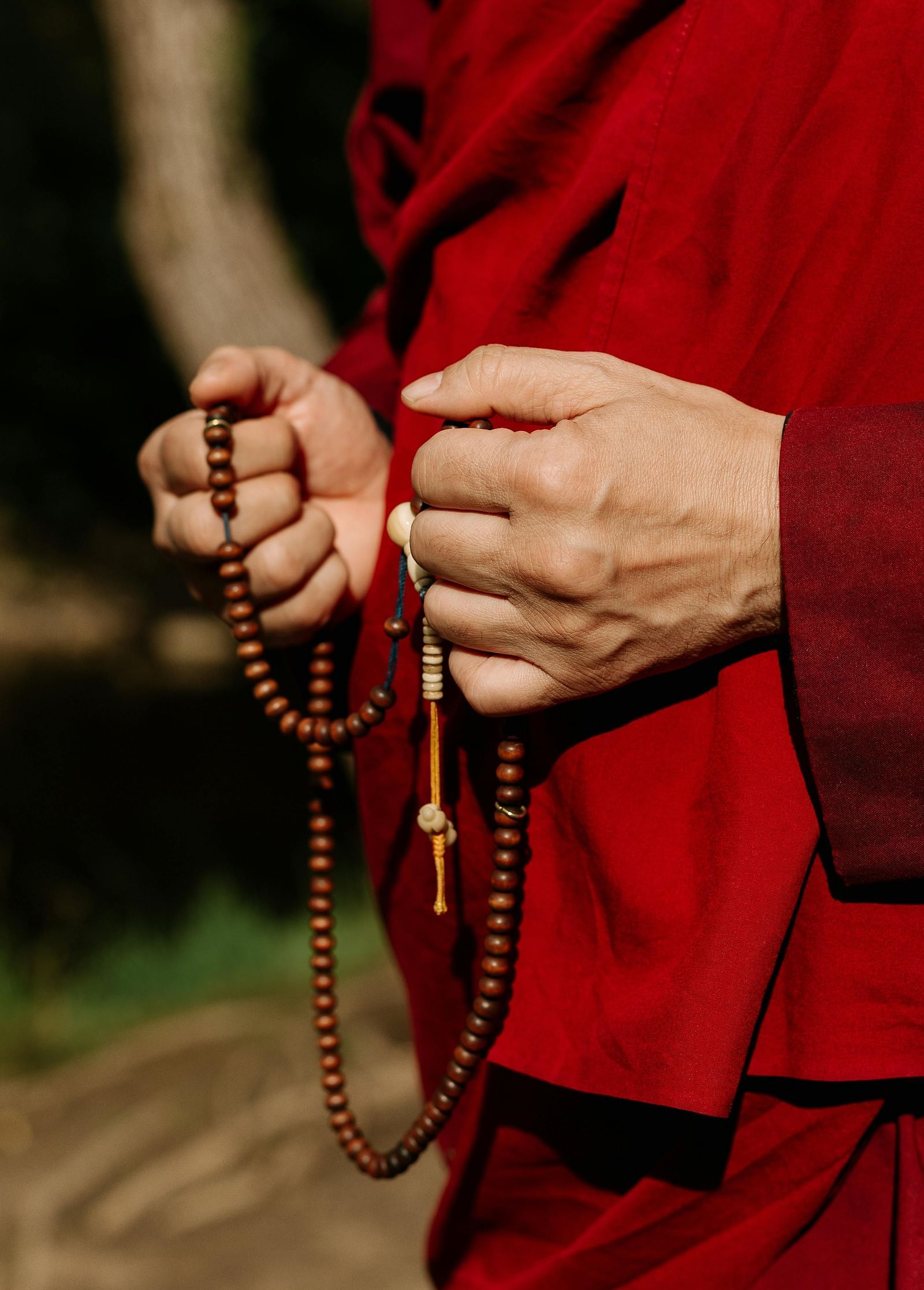 The hands and body of a buddhist monk can be seen wearing his robes and carrying prayer beads in his both hands.