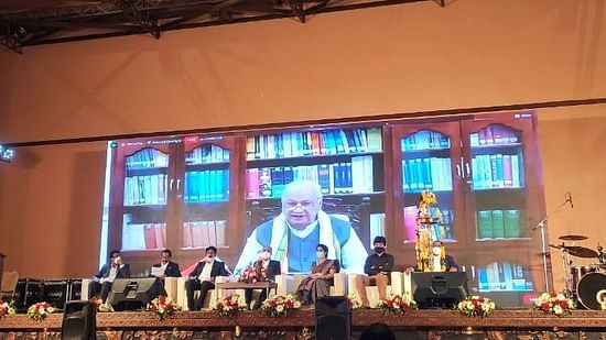 A renowned public figure giving speech on a large projector on the stage as the rest of the members are sitting on the chairs at Uday Palace Convention Centre