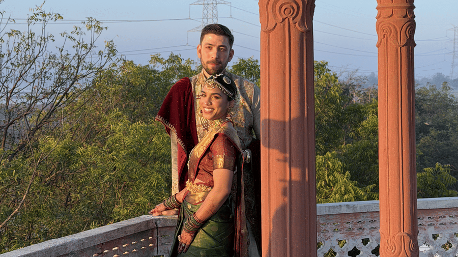A couple in traditional attire stands by carved stone pillars on an elevated balcony overlooking trees at Umaid Palace.